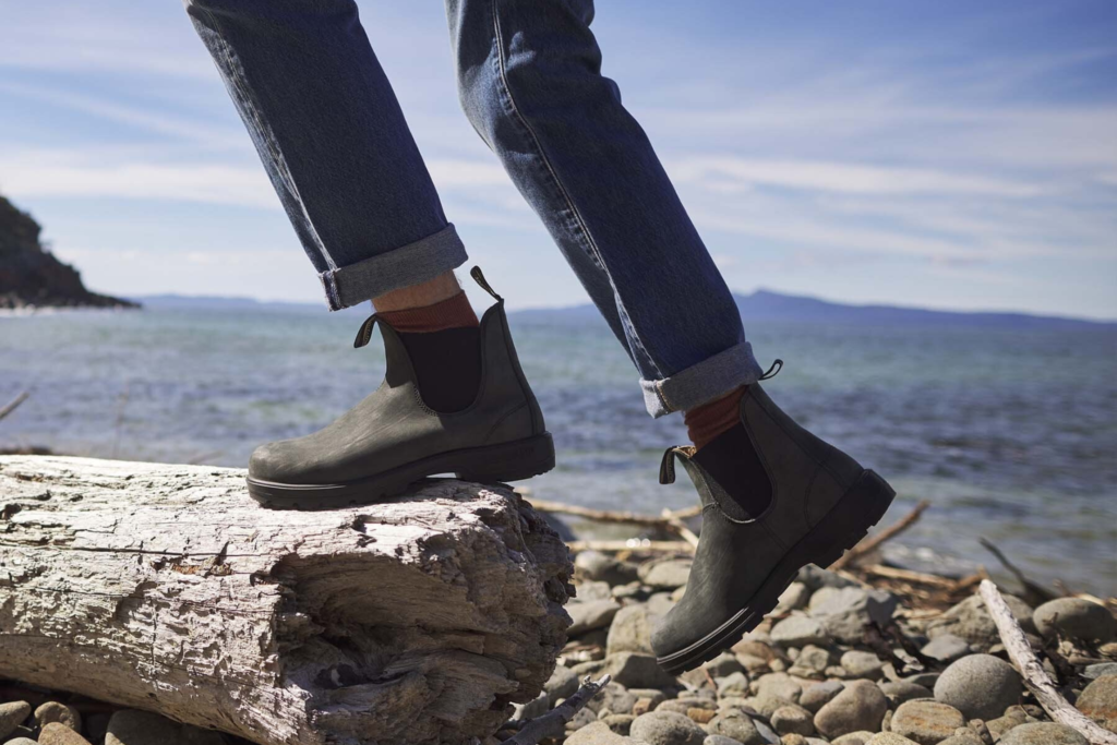 a man wearing blundstone shoes on a pebble beach